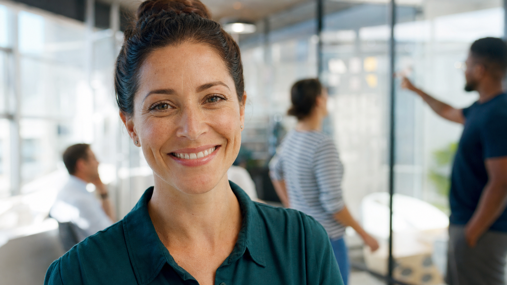 Smiling team lead looking at camera as her team collaborates behind her, showing teamwork makes the dream work