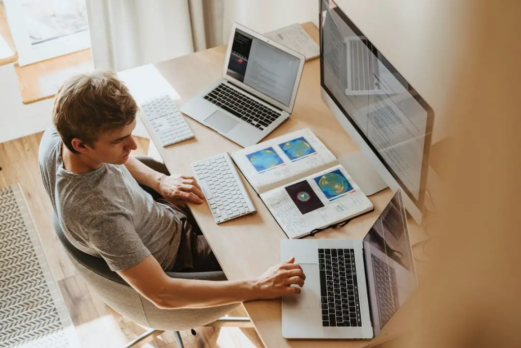 A man sitting in front of three laptops working from home.