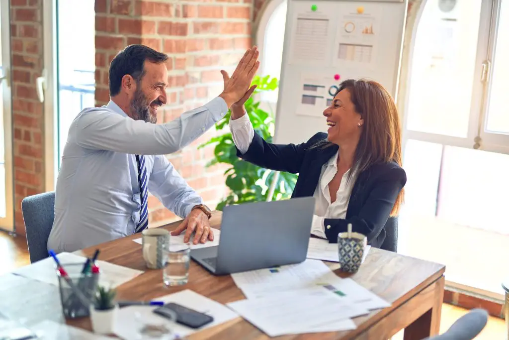 Two middle age business workers smiling happy and confident. Working together with smile on face hand giving high five at the office. Interpersonal Communication Skills 