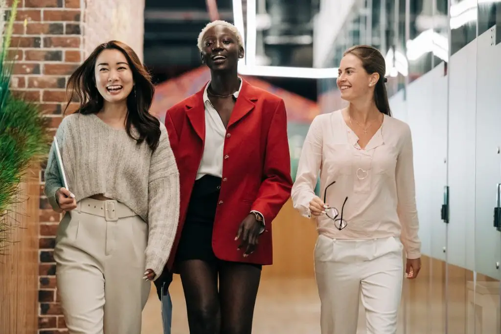 Diverse elegant multiracial businesswomen walking in a contemporary office smiling. Communication competence. 