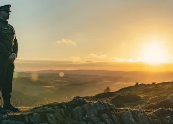 a stern-faced officer stands proudly atop a sunlit hill, gazing out into the distance with unwavering determination.